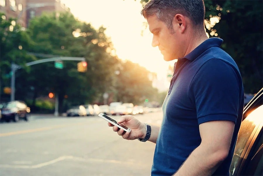image of a man looking down at his smartphone leaning up against a car